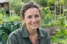 Portret van een lachende vrouw met opgestoken haar en groen werkhemd in een moestuin met boerenkool